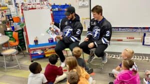Two Fargo Force players reading to students in a classroom