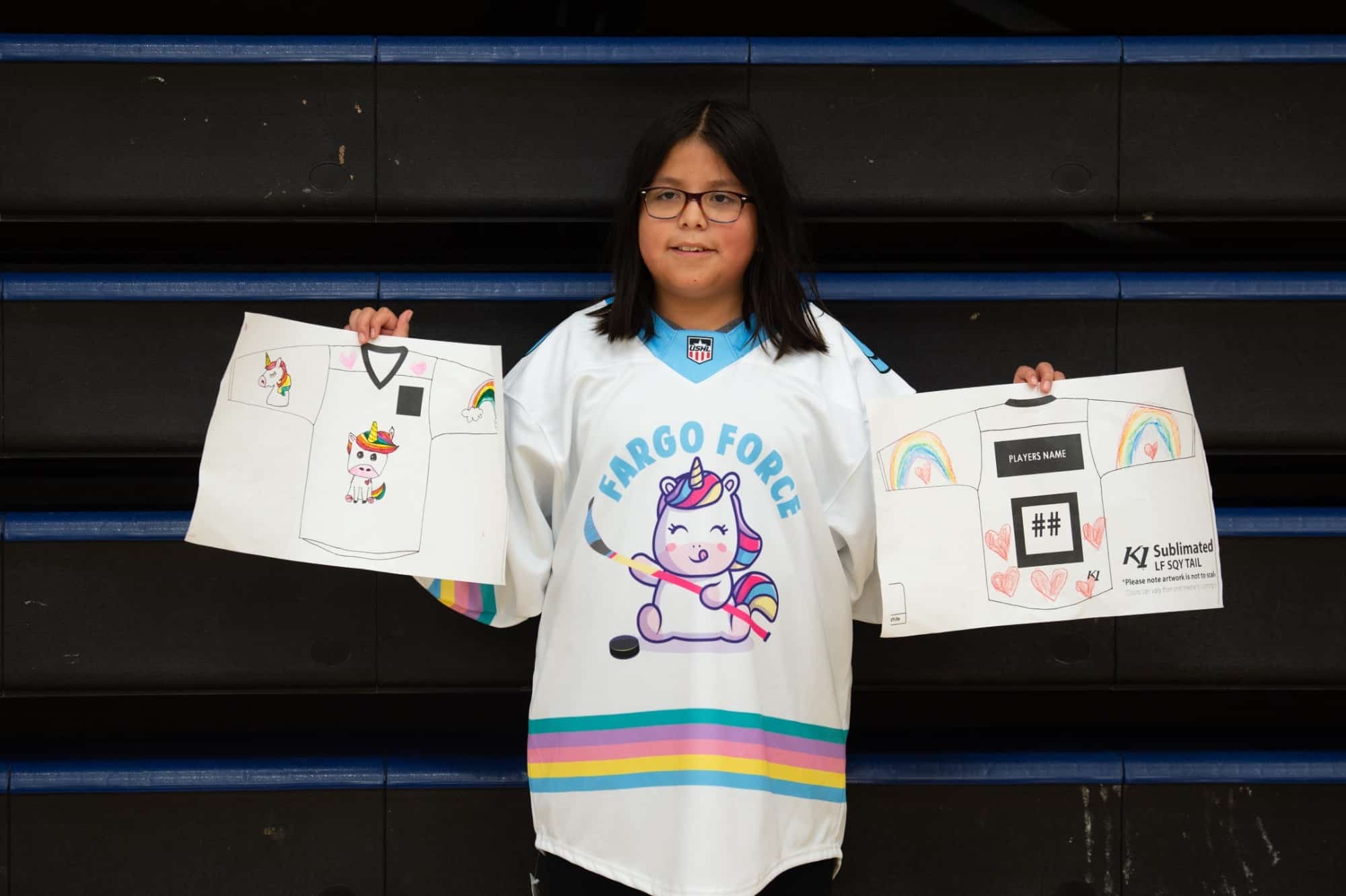 Charleigh holding up her Fargo Force Jersey drawings.
