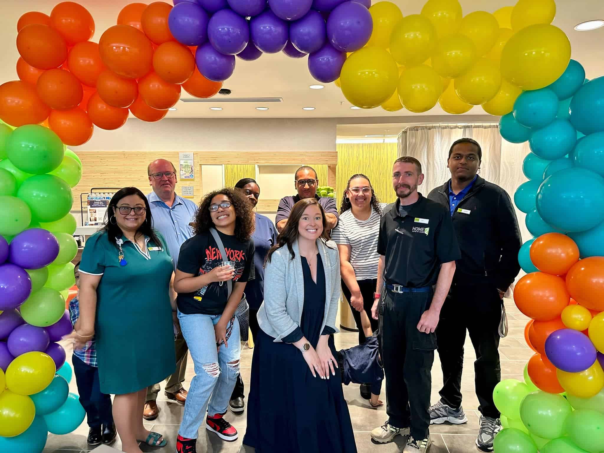 The staff of Home2 Suites by Hilton, Poughkeepsie smiling and standing under a balloon arch.