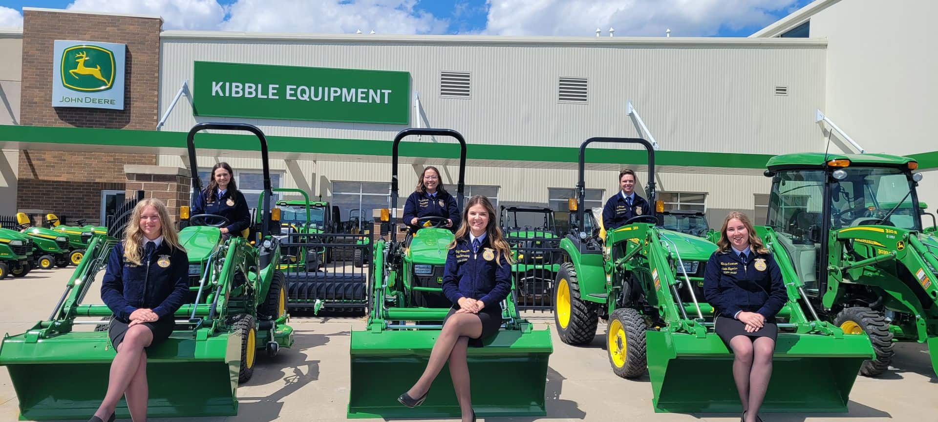 MN FFA Foundation State Officers sitting on equipment in front of Kibble Equipment