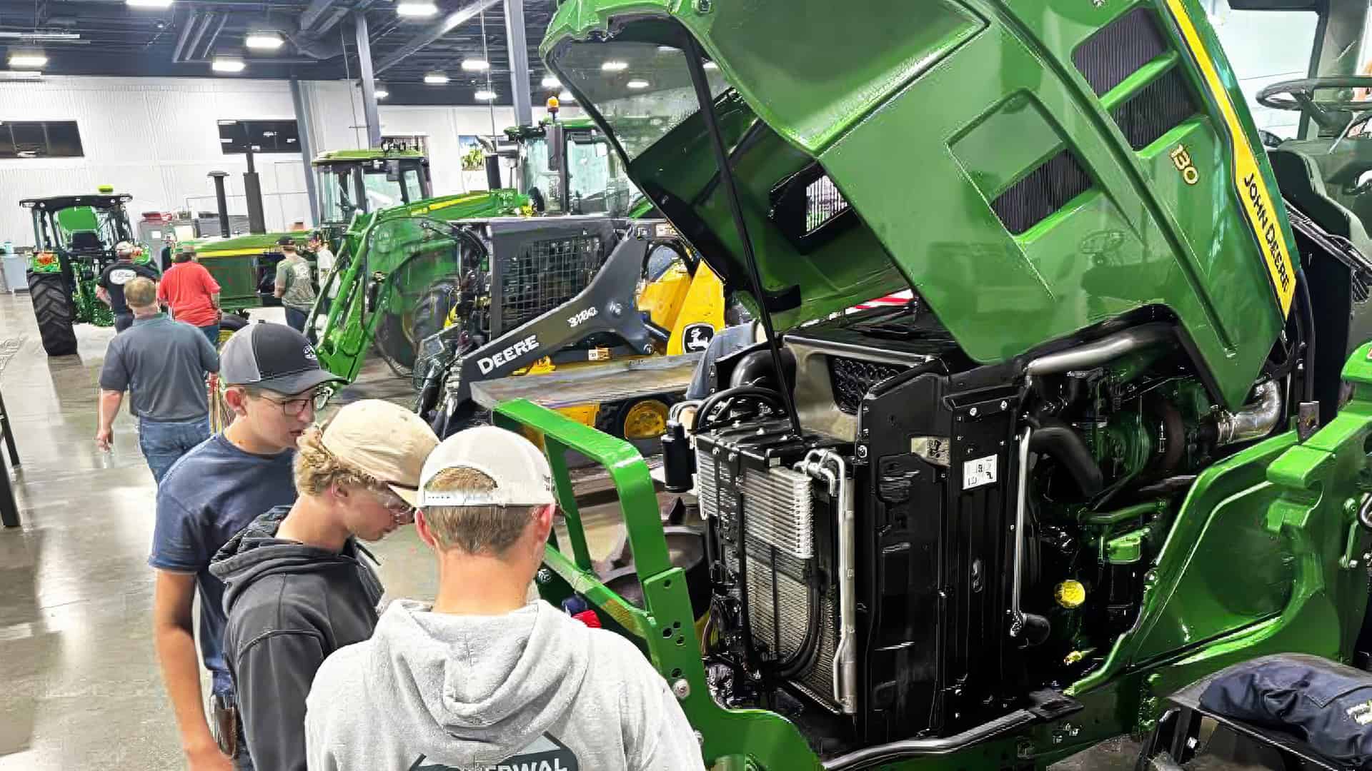 Three young looking down accessing an engine of a John Deere tractor during diesel camp.